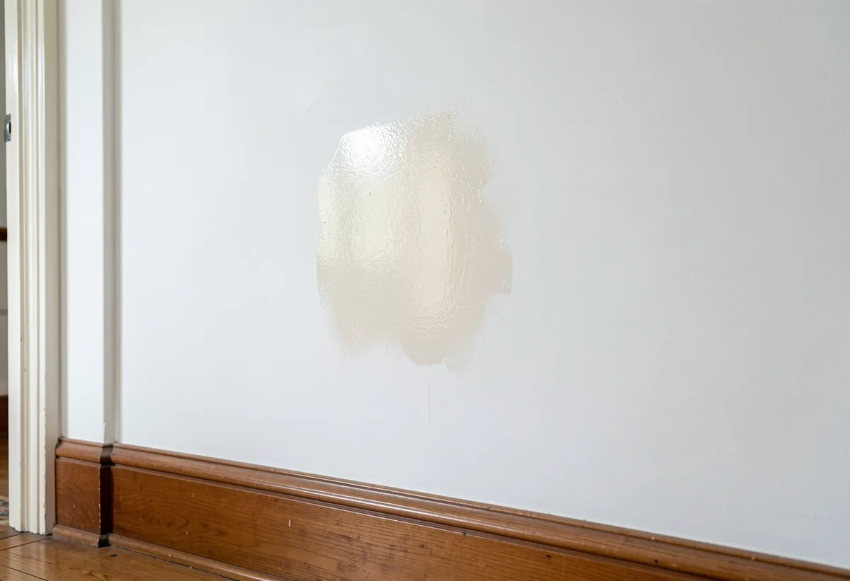 White wall with a faint shiny burnished patch where a mark was scrubbed on matte paint.