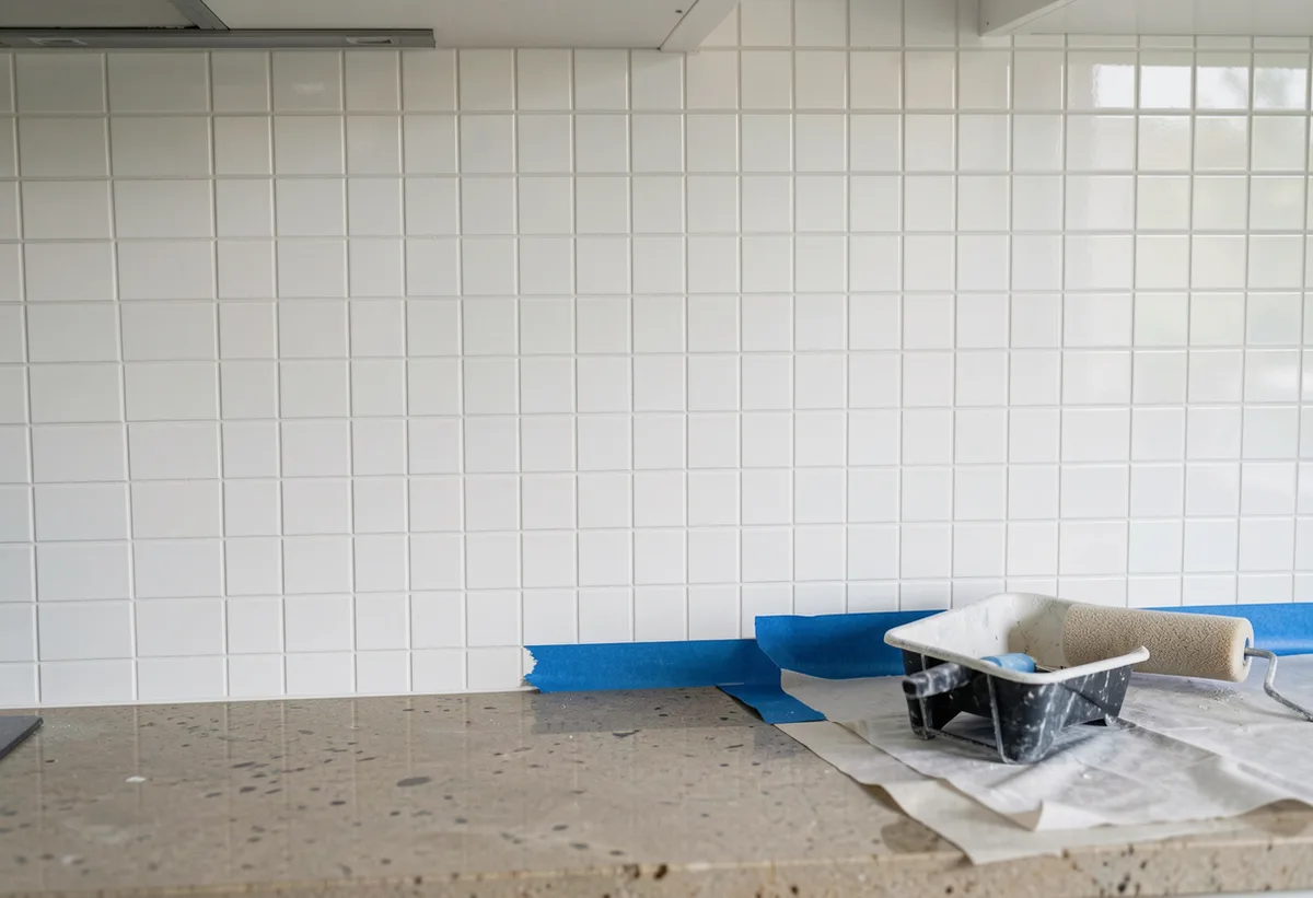 Freshly painted white splashback tiles behind a kitchen bench, painter's tape being removed to show a clean edge.