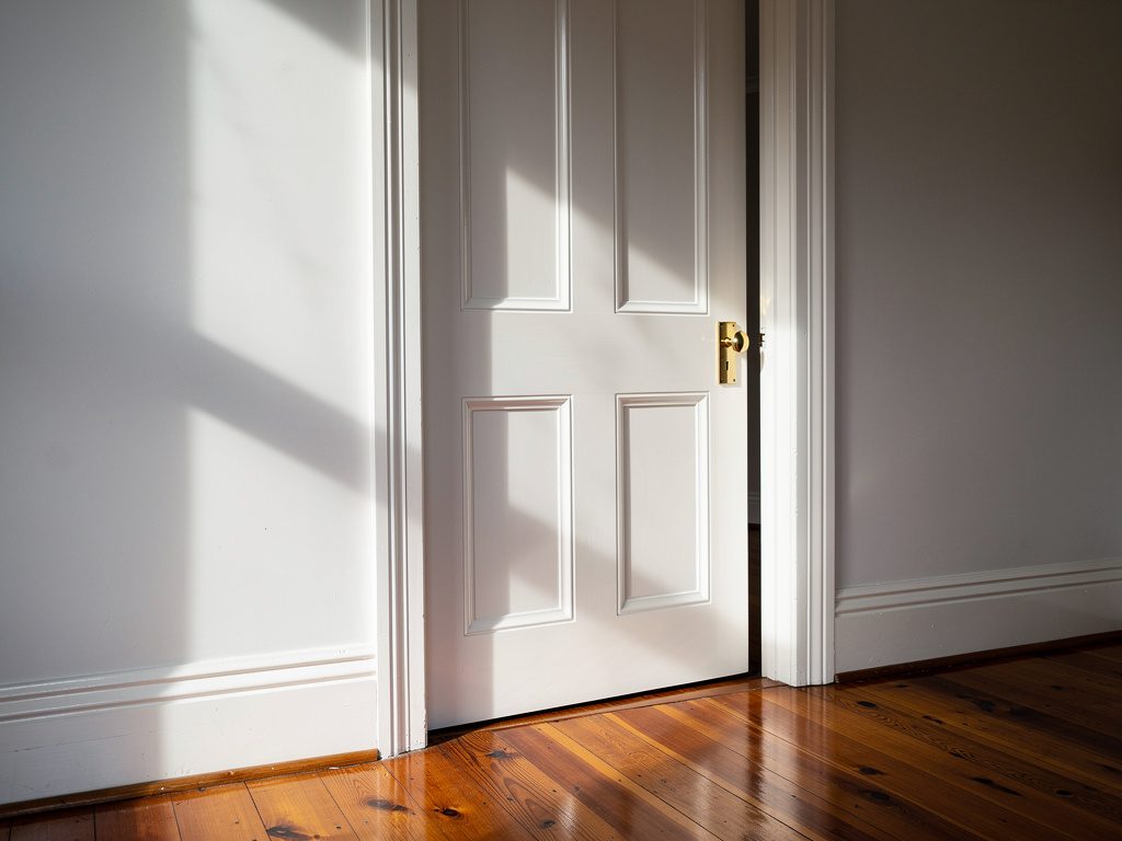 Freshly painted white four-panel internal door with brass knob, heritage cornice and polished hardwood floors in a Footscray period home