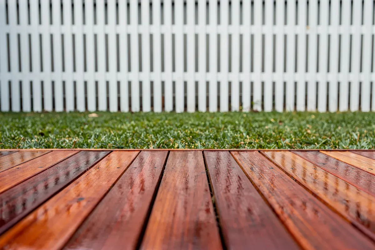 Freshly oiled timber decking boards beside a white picket fence and lawn
